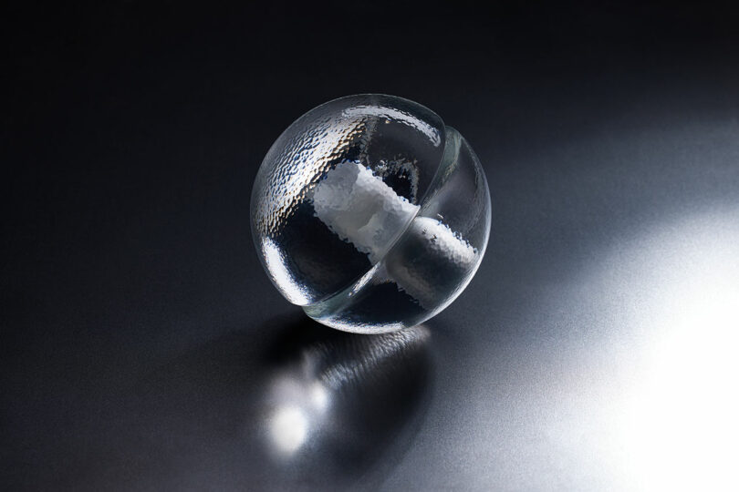 A clear glass sphere with a frosted cylindrical section inside, the Bocci 14p rests elegantly on a dark reflective surface under focused lighting.