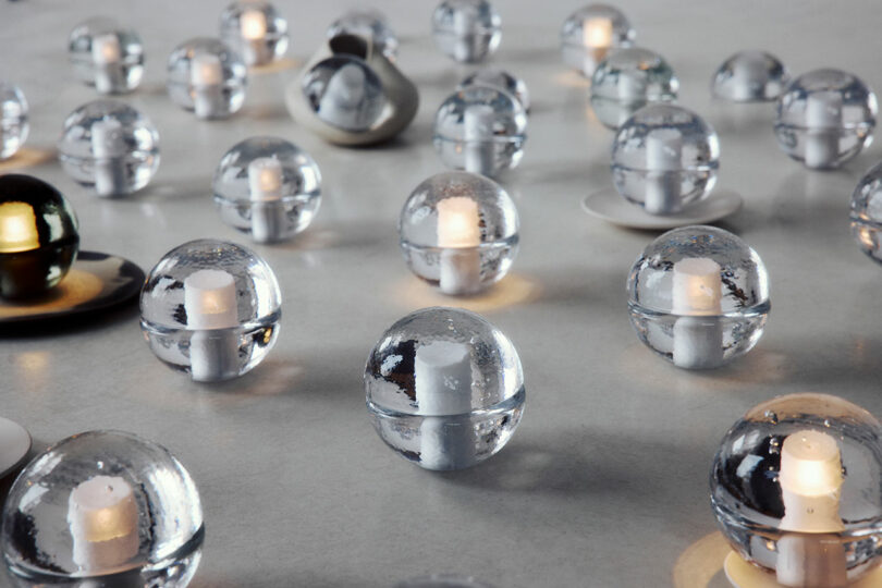 Several transparent glass spheres, reminiscent of the Bocci 14p design, each containing a small candle-like light, are arranged on a smooth, light-colored surface.