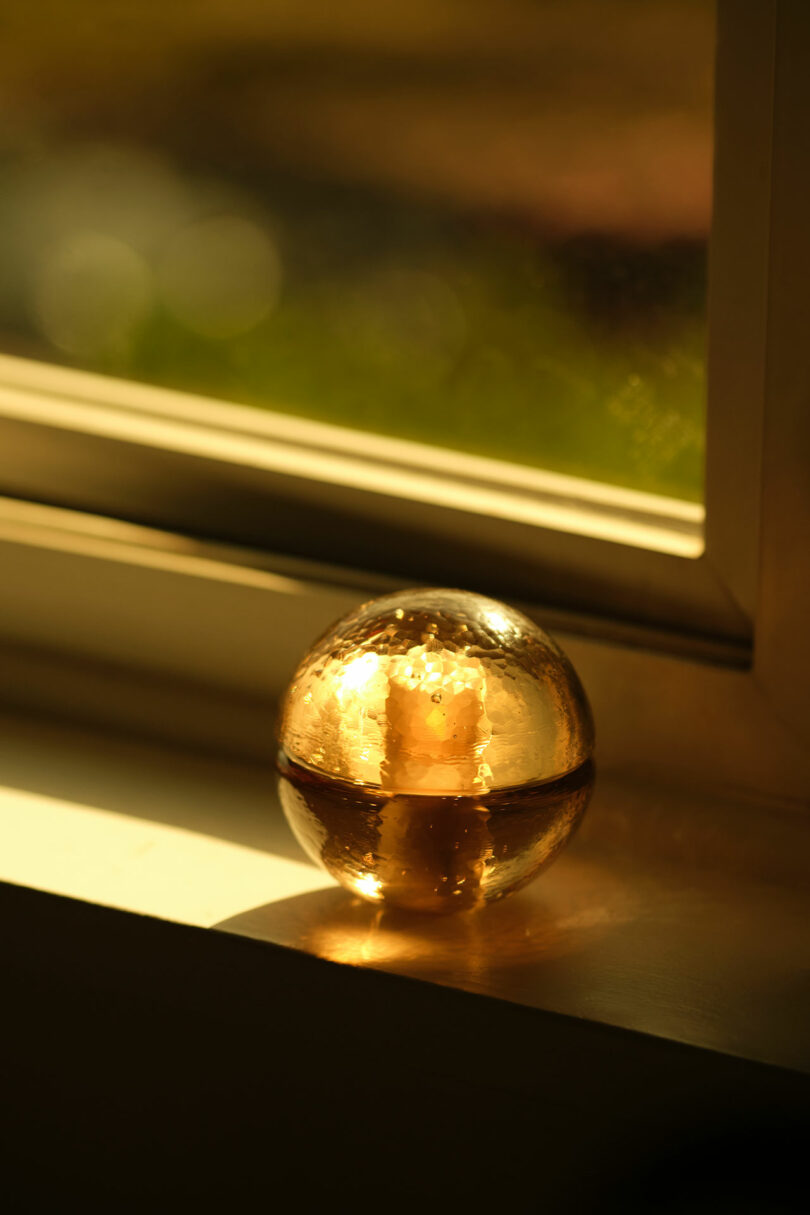 A Bocci 14p glass sphere with air bubbles inside sits on a windowsill, illuminated by warm sunlight.