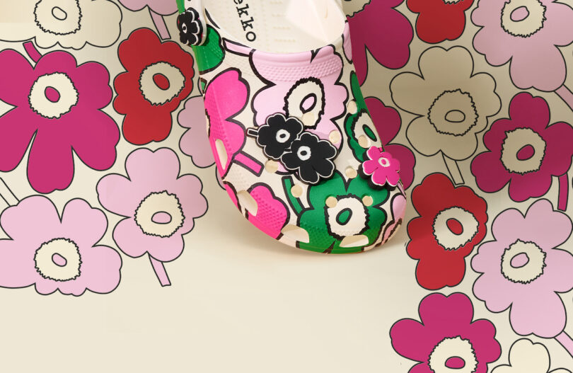 A shoe with a bold floral pattern, featuring pink, red, green, and black, blends into a matching flower-patterned background.