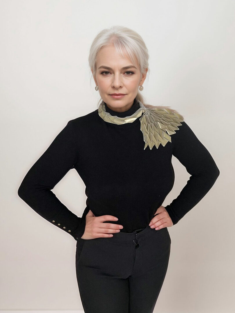 A woman with light hair in a black outfit poses with hands on hips, showcasing a metallic decorative accessory from the 3Dtachables Collection on her shoulder, against a plain white background.