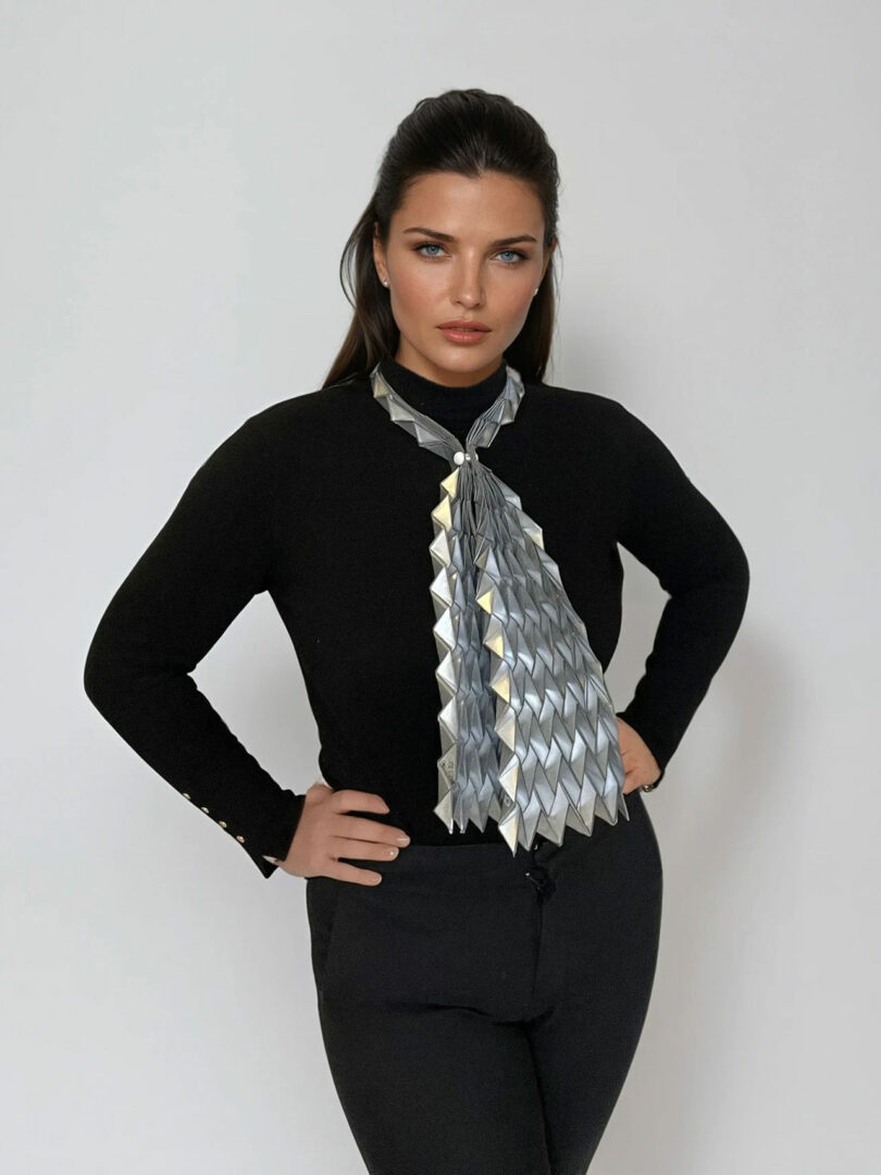 Woman standing against a plain background, wearing a black outfit and a large, geometric metallic scarf with an origami-like design by Liat Brandel.