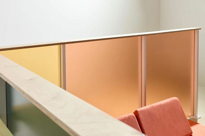 Two orange chairs are placed next to pastel-colored 3form partition panels in a minimal, modern interior space.