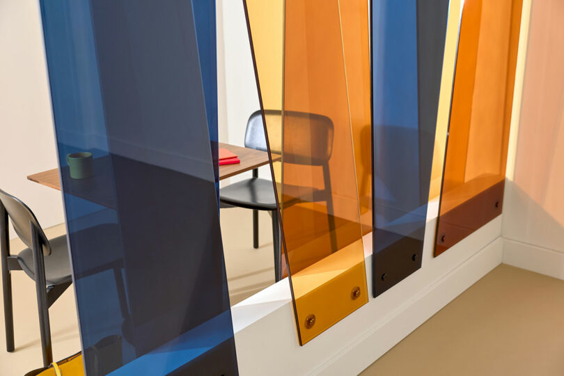 A modern office space with a table, two chairs, and colorful translucent blue and orange 3form partitions separating the area.