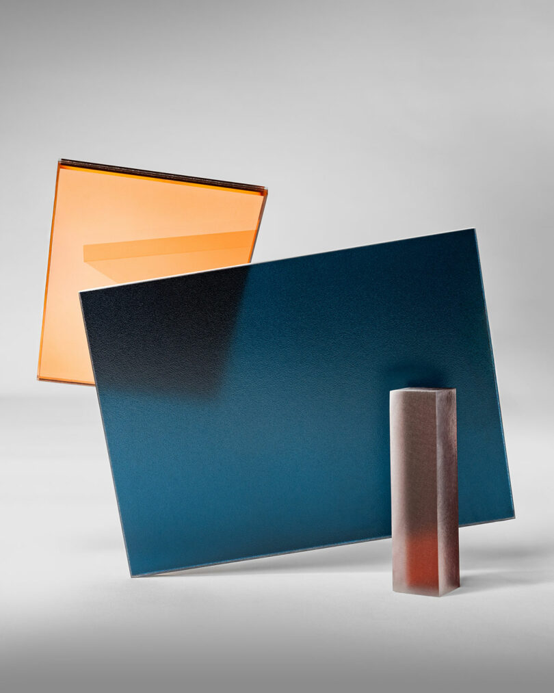 Three geometric 3form glass objects—an orange-edged square, a blue rectangular sheet, and a small frosted rectangular block—stand against a neutral background.