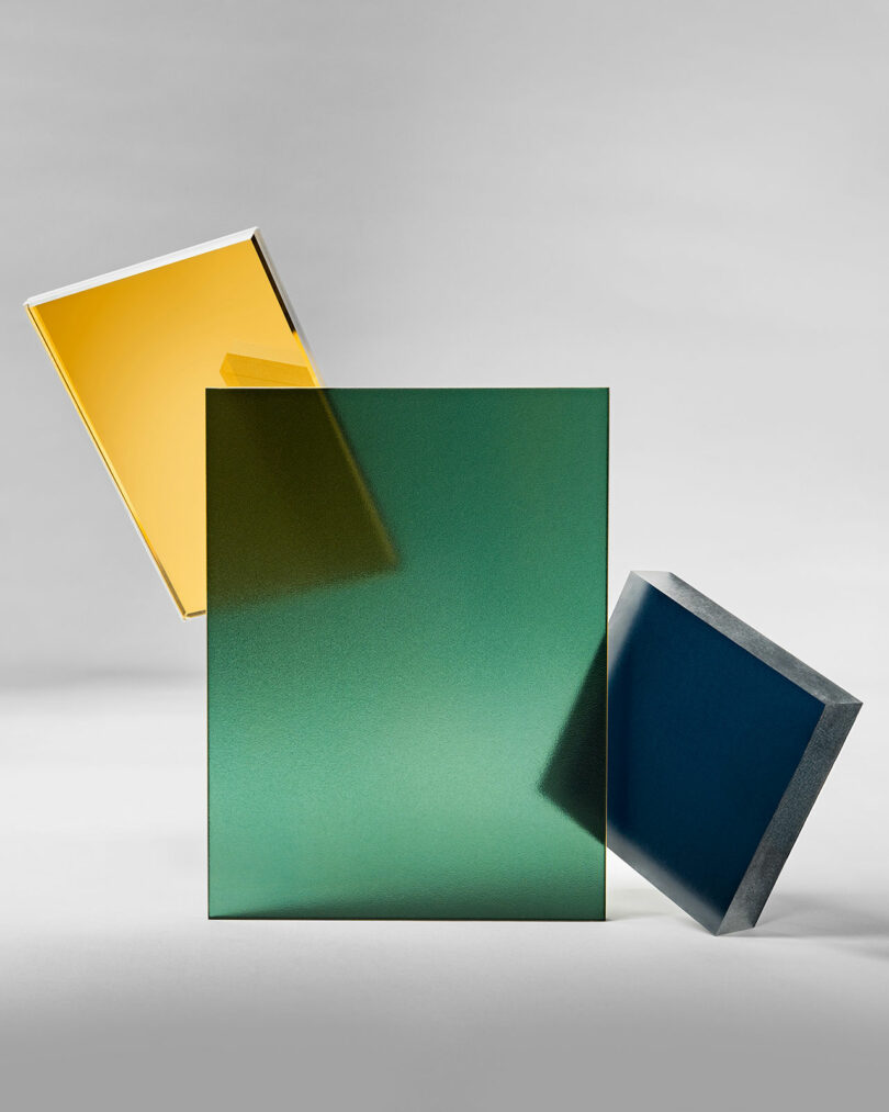 Three opaque geometric panels—yellow, green, and blue 3form surfaces—are arranged against a neutral background, with one panel upright and the other two slightly tilted.