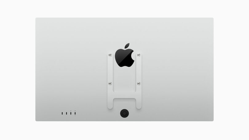 Rear view of an Apple monitor showing the Apple logo, VESA mount adapter, ports, and a central circular cutout.