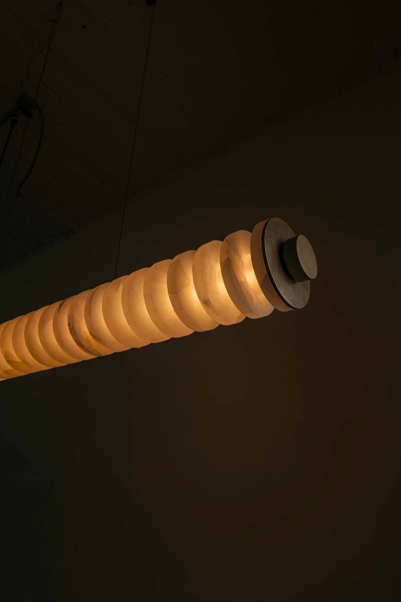 An ATRA cylindrical hanging light fixture with a segmented, spiral design glows warmly against a dark background.