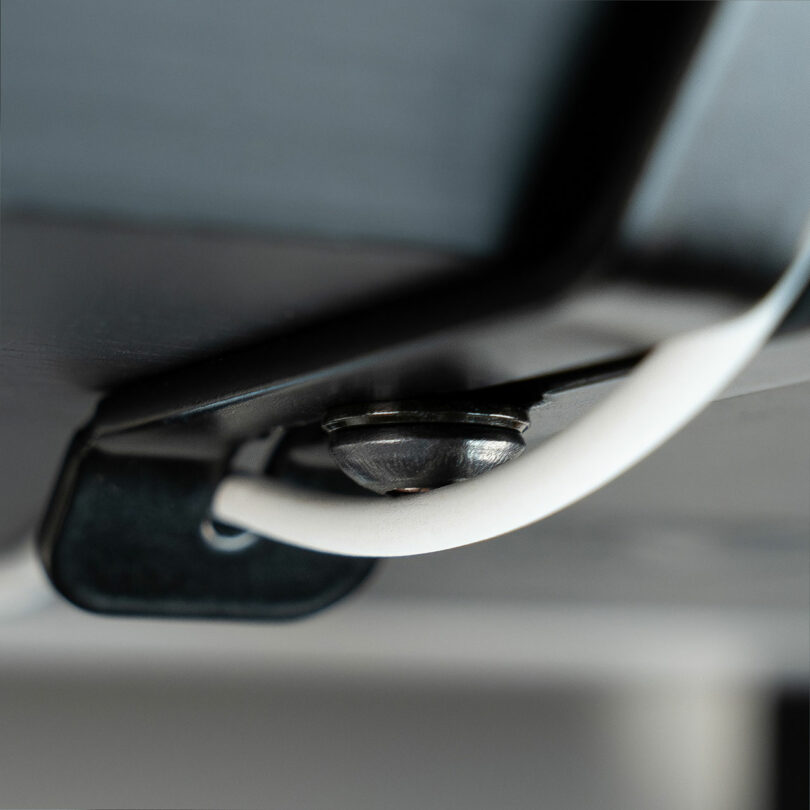 Close-up view of a white cable routed through a black Balolo clip and secured by a metal screw.