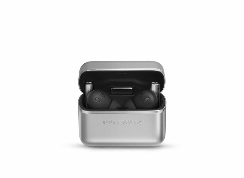 A pair of black wireless earbuds in a silver charging case, with the lid open and "Bang & Olufsen" logo visible on the front.