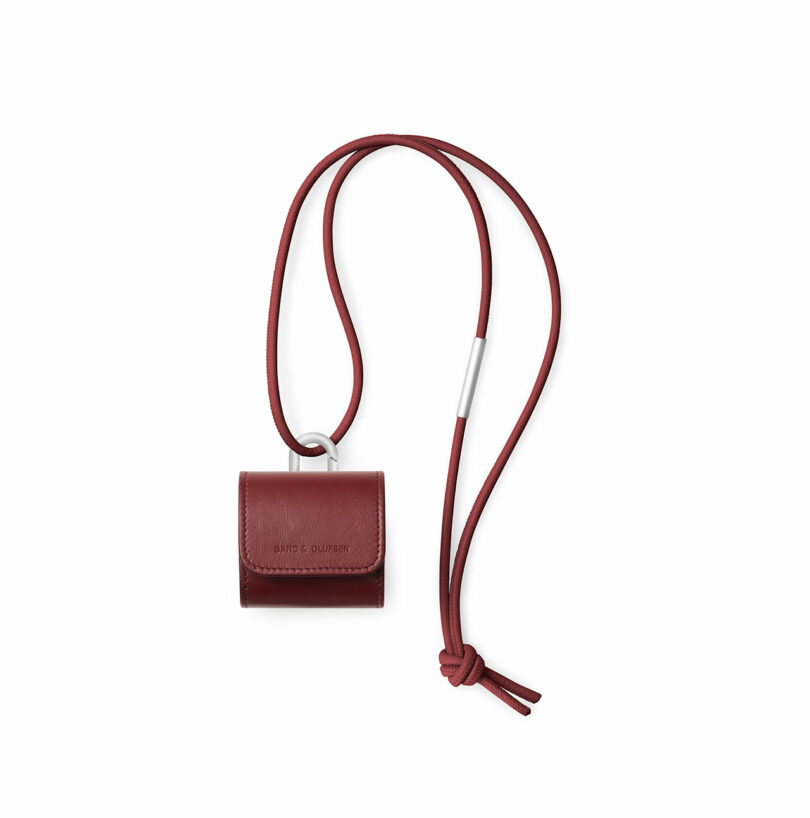 A small burgundy leather case with a flap closure and embossed text, attached to a matching adjustable neck strap with a knotted end and metal accent.