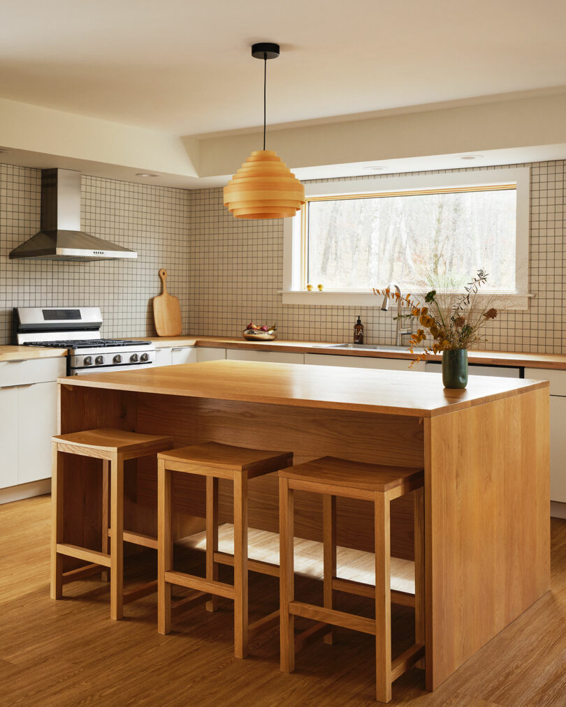 Modern kitchen featuring a wood island and stools, Design Within Reach-inspired white cabinetry, tiled backsplash, stainless steel appliances, and a large window above the counter.