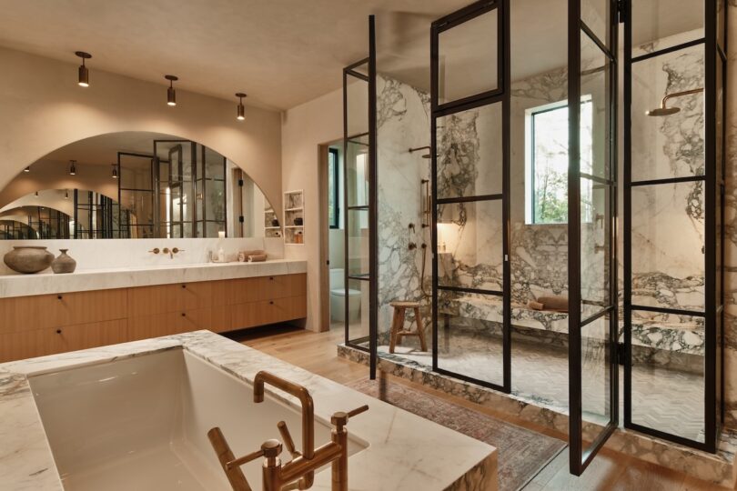 Modern bathroom with marble finishes, a glass-enclosed shower, freestanding bathtub, wooden cabinetry, and warm ambient lighting.