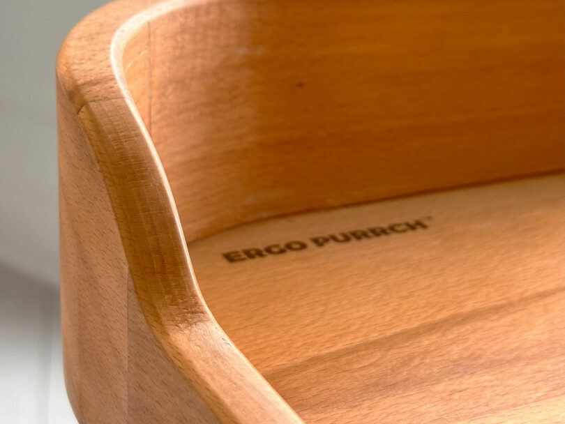 Close-up of the Ergo Purrch wooden object, featuring smooth, curved edges and the words "ERGO PURRCH" elegantly engraved on its surface.