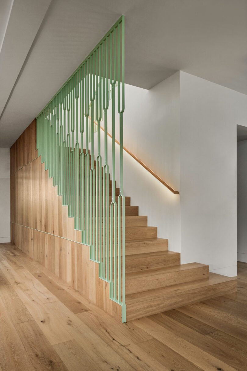A modern staircase with wooden steps and a light green geometric metal railing, part of a Friday 5–inspired minimal interior featuring white walls and sleek wood paneling.