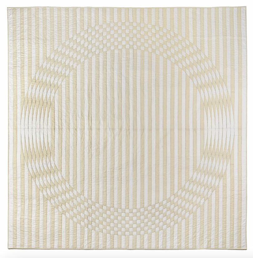 A quilt with a geometric design featuring vertical beige and white stripes, intersected by a large, circular pattern of alternating light and dark blocks inspired by Vivian Chiu's distinctive style.