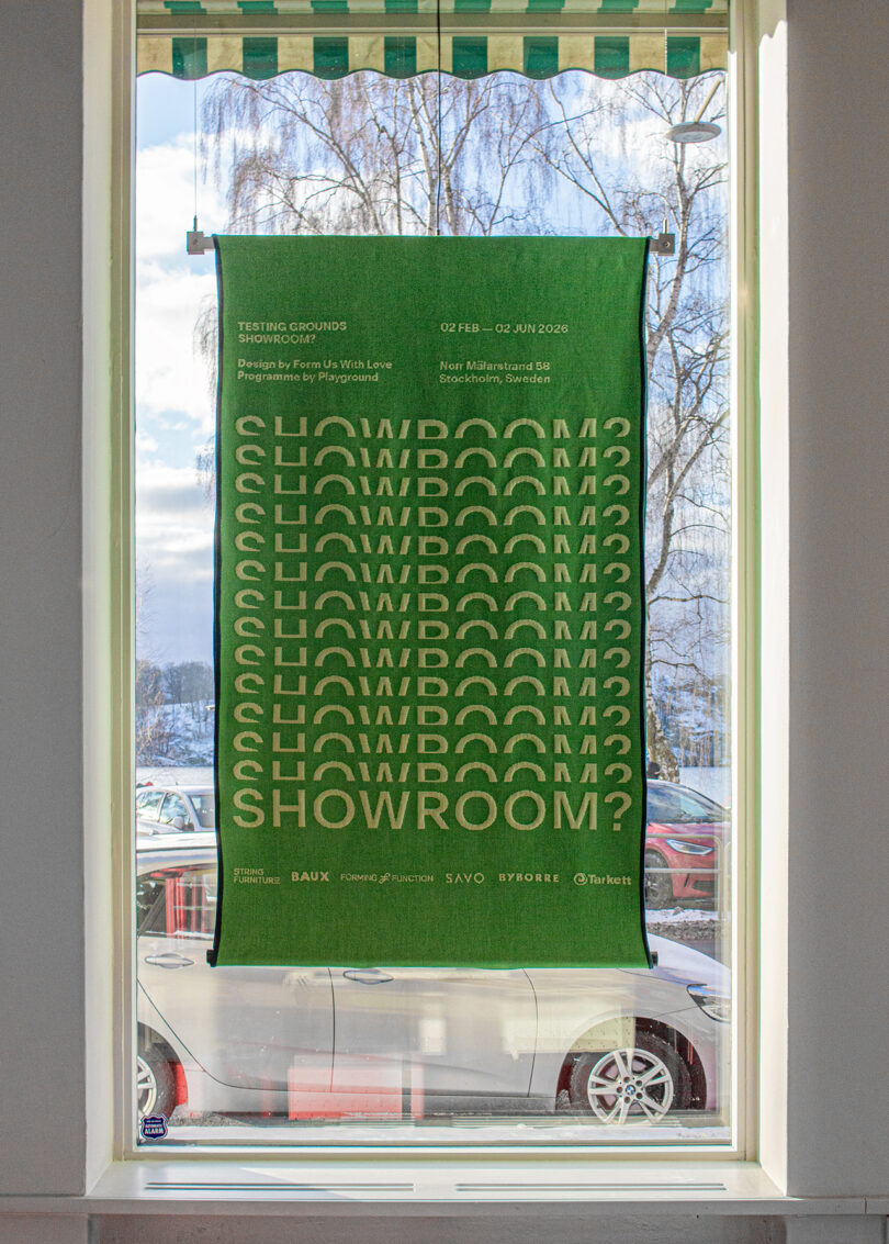 A green poster by Form Us With Love with repeated text "SHOWROOM?" hangs in a window, with cars and a snowy outdoor scene visible outside.