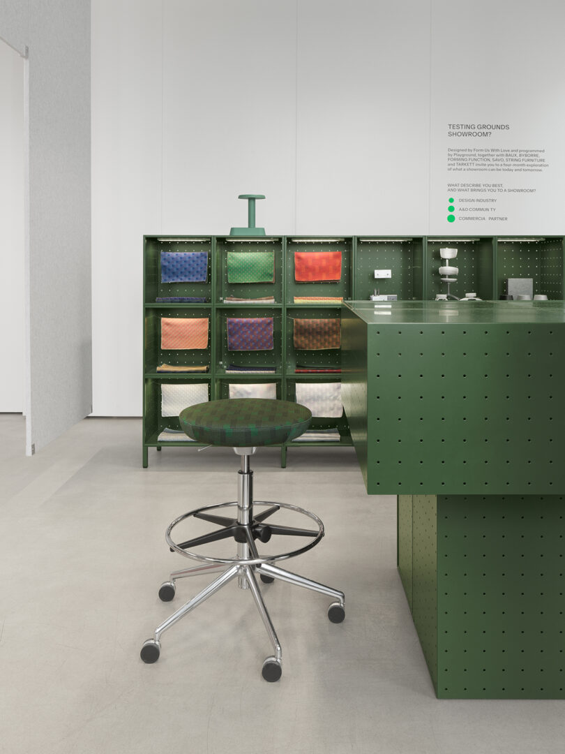 A green office chair with wheels sits in front of a green pegboard counter and cubby shelves holding colored folders in a modern, minimalist office space designed by Form Us With Love.