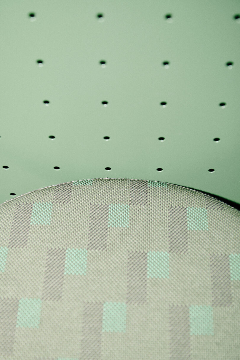 A close-up of a fabric cushion with a geometric pattern beneath a green perforated surface, featuring evenly spaced small holes—a design inspired by Form Us With Love.