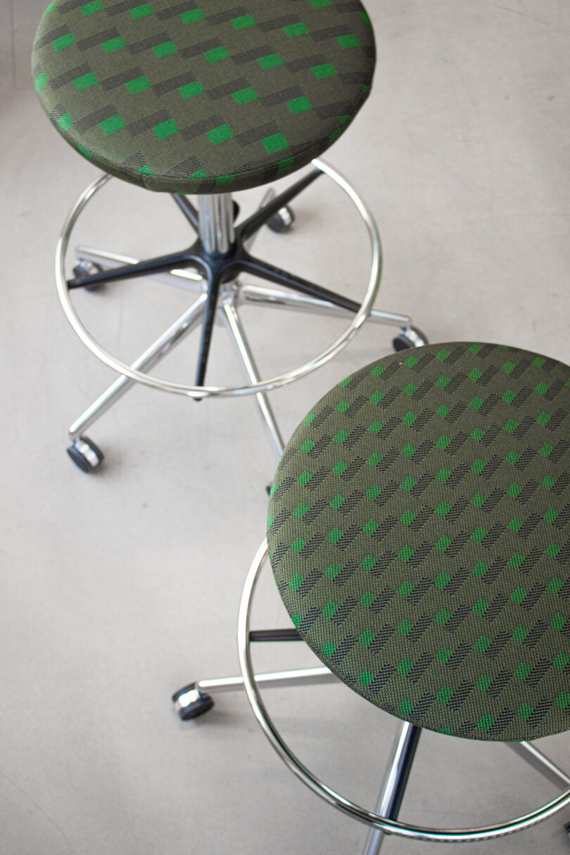 Two round stools with chrome bases and casters, upholstered in green and grey patterned fabric with different geometric designs—showcasing a style reminiscent of Form Us With Love.