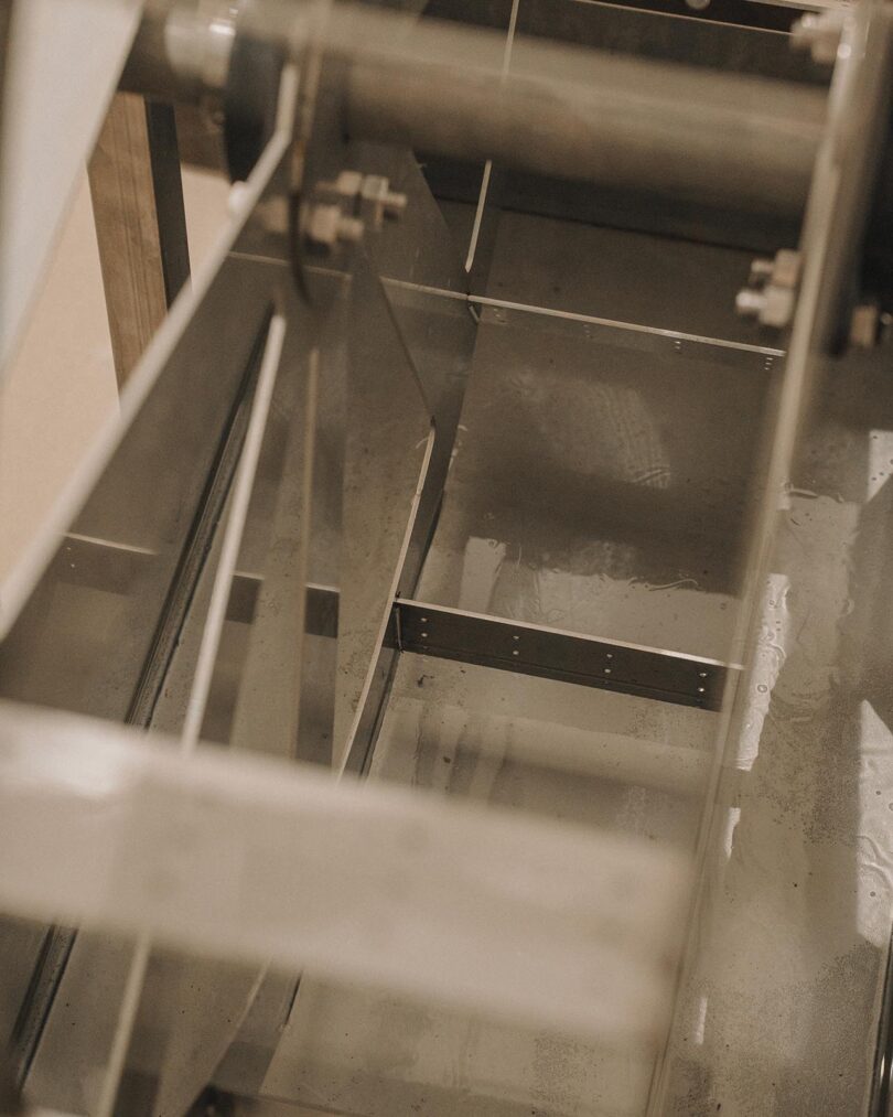 Close-up of a metal industrial machine with gears, bolts, and reflective surfaces, showing part of its inner mechanical structure.