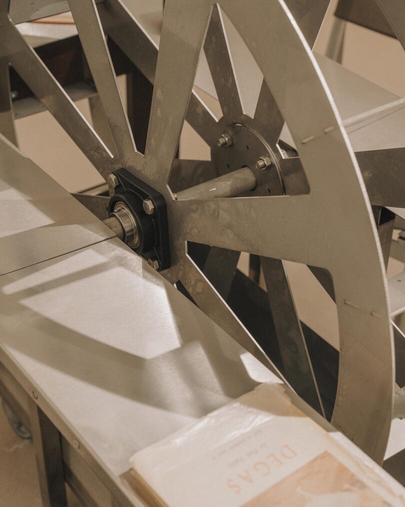 Close-up of a metal wheel mechanism on a machine, with part of an open book labeled “IDEAS” visible in the foreground.