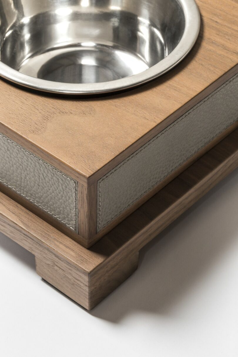 A close-up view of a metal pet food bowl fitted into a modern wooden stand with textured panel detailing
