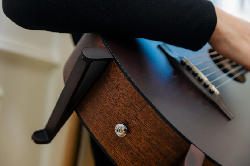 Close-up of a person resting their arm on the body of a wooden acoustic guitar, focusing on the instrument's side and strings.