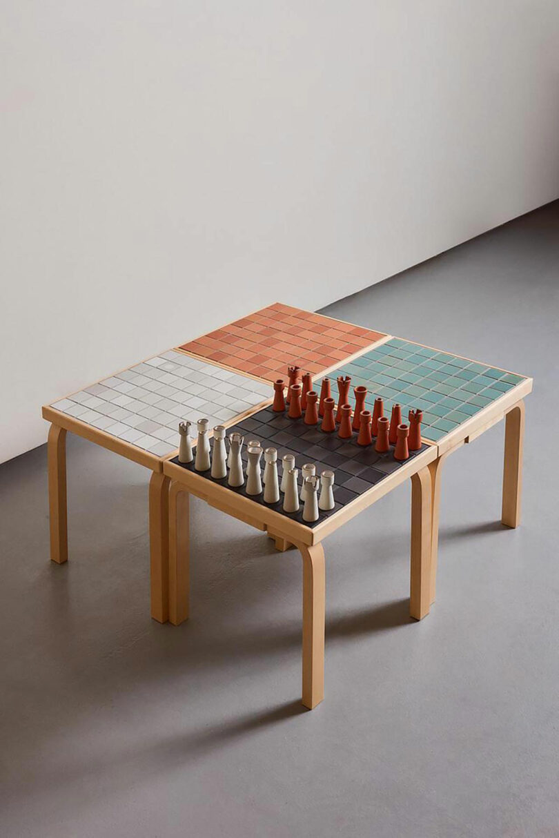 A wooden Artek table with four different colored tiled sections, featuring a chessboard and chess pieces arranged for a game.
