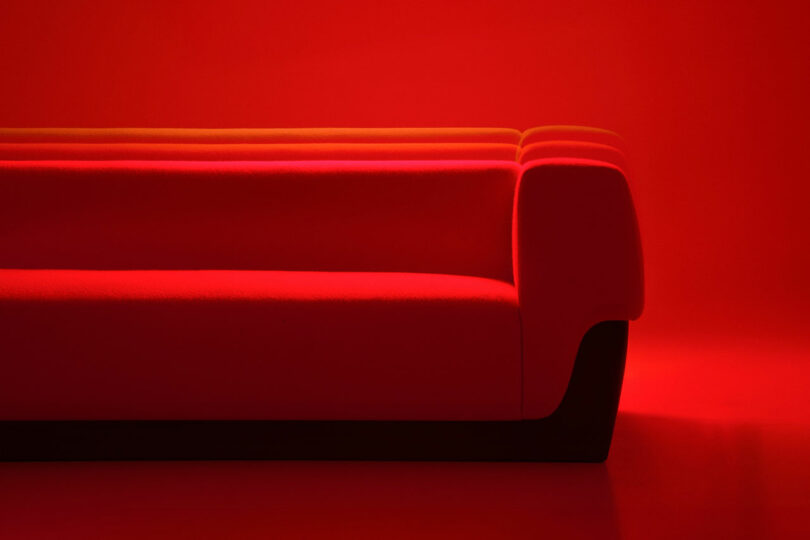 Red modern sofa from Holly Hunt against a red background, photographed from the side with dramatic lighting that creates distinct shadows and highlights.