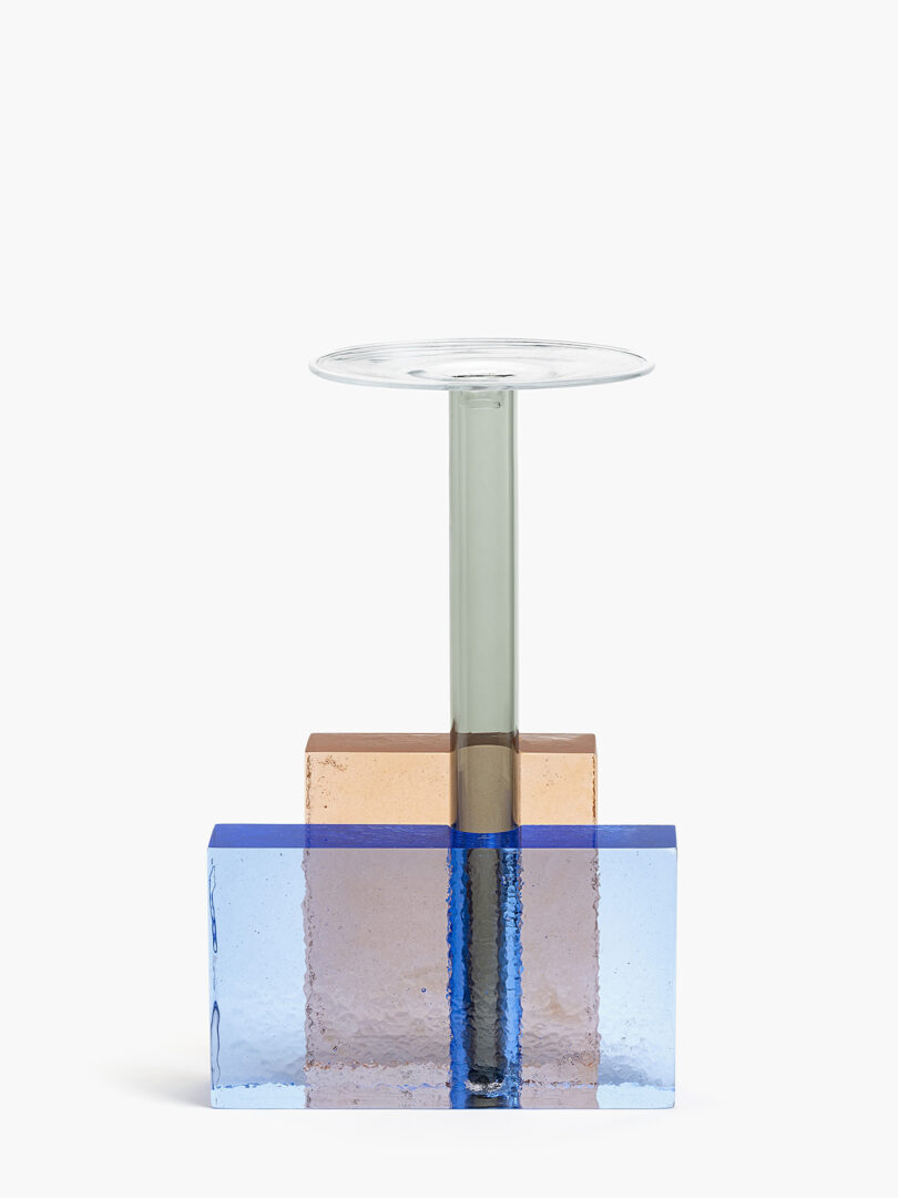Glass sculpture composed of a round clear top, a green vertical stem, and intersecting blue and amber rectangular bases.