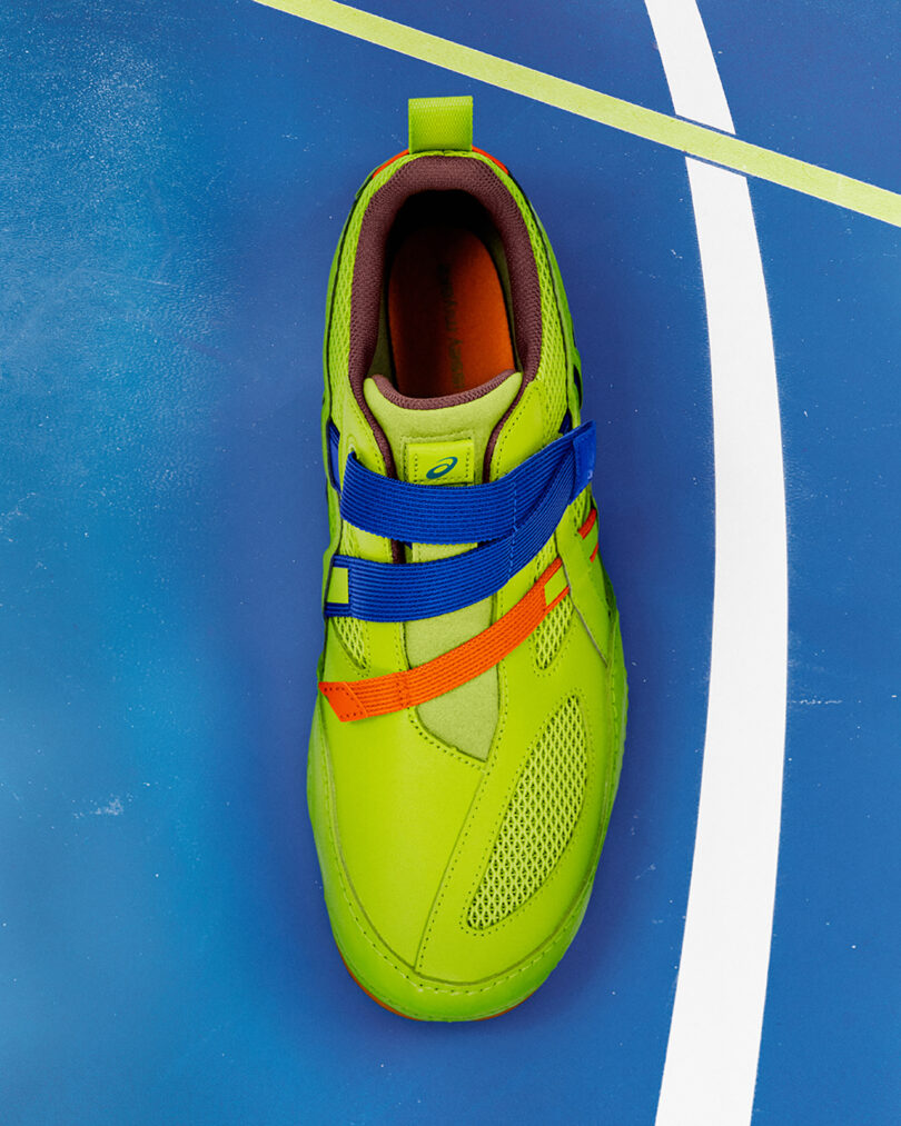 A single neon green athletic shoe with blue and orange straps is placed on a blue surface with white and yellow lines.