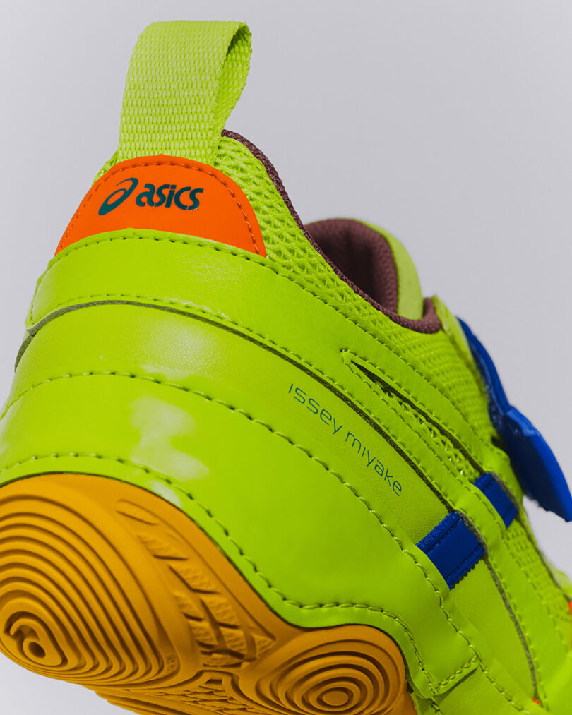 Close-up of a neon green Asics sneaker with blue accents, orange and yellow detailing, and "issey miyake" printed on the side.