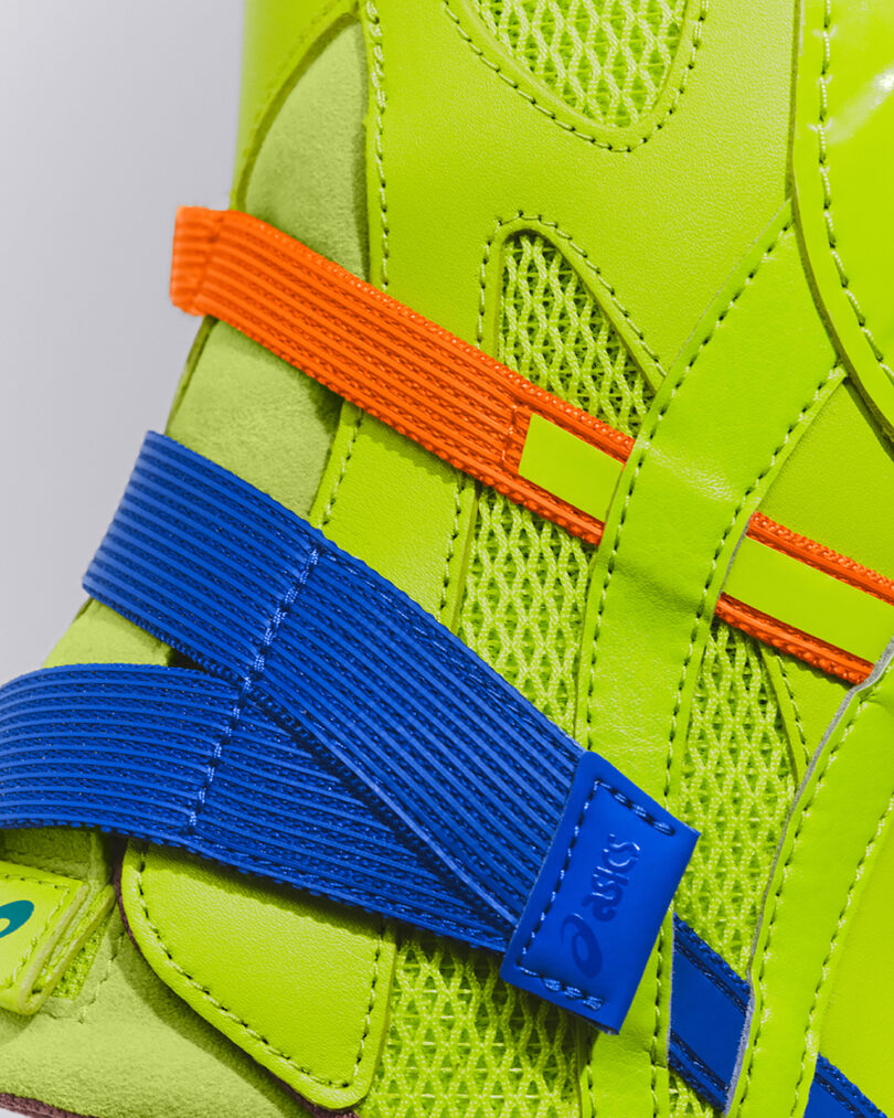 Close-up of a neon green shoe with orange and blue textured straps, mesh fabric, and visible stitching detail.