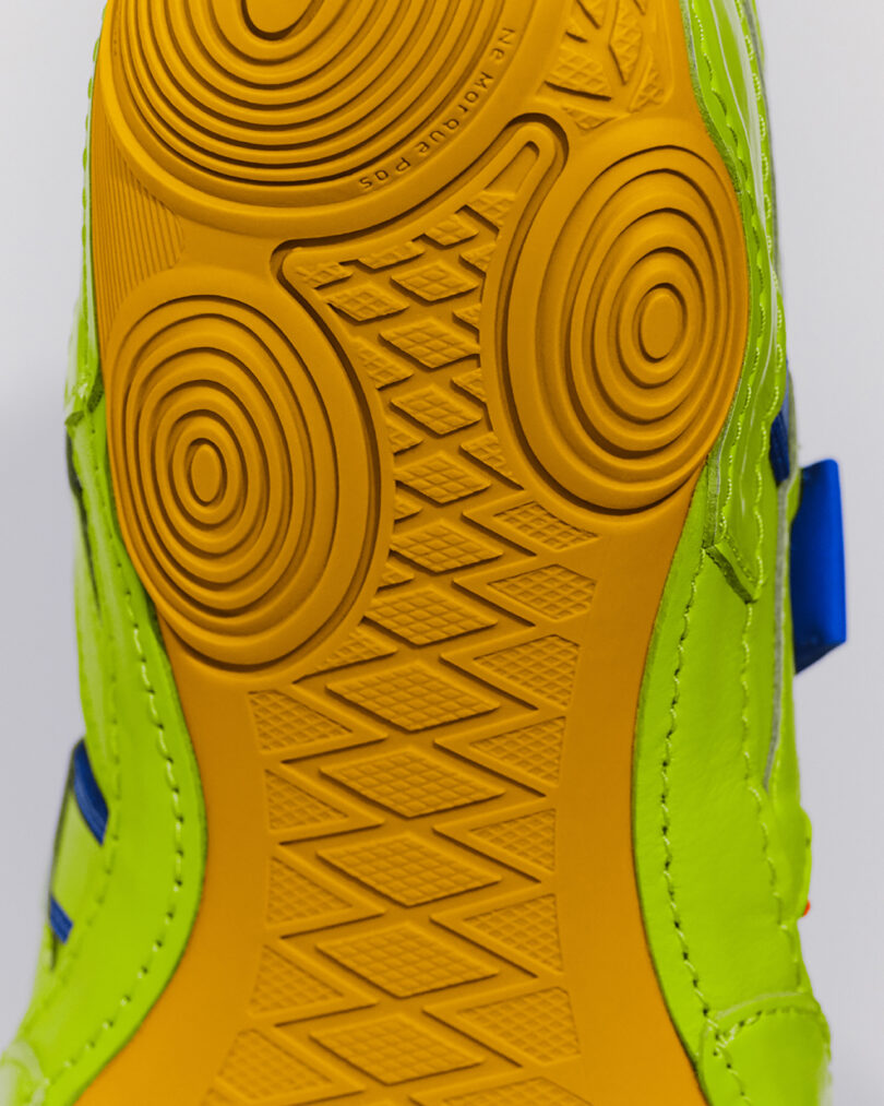 Close-up view of the yellow and green sole of a shoe, showing circular and diamond tread patterns for traction.