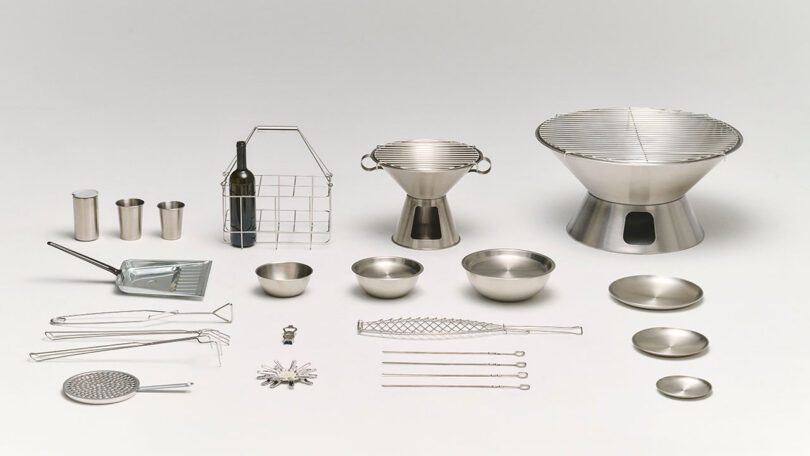 A collection of stainless steel barbecue utensils, grills, bowls, plates, skewers, tongs, and a wine holder arranged on a white background.