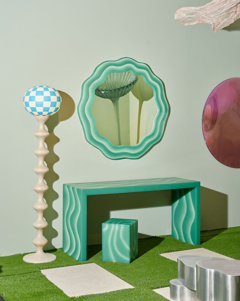 A room with green wavy-edged mirror, matching desk and stool, checkerboard floor lamp, round wall art, and grass-textured flooring with stone-like platforms.