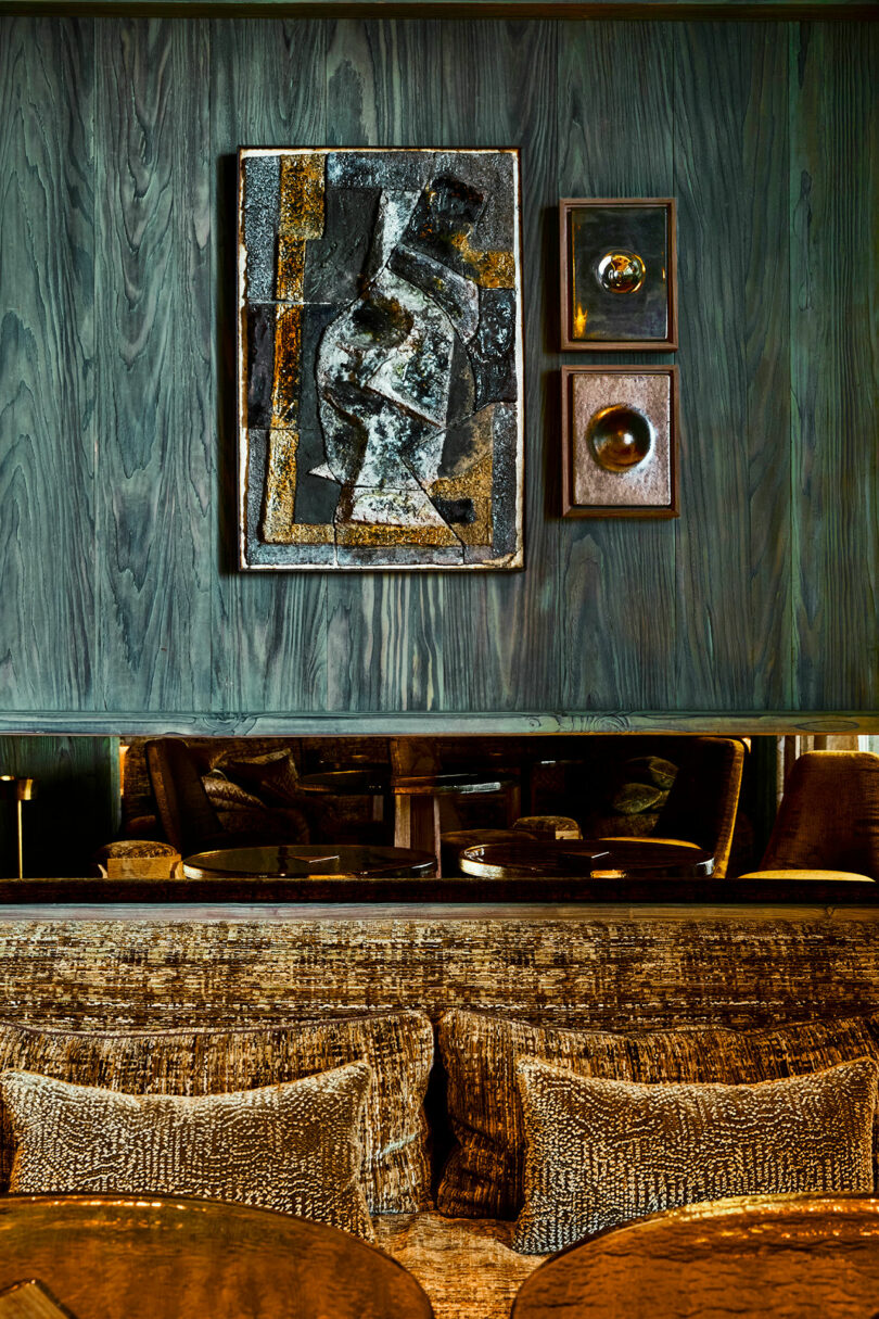 A cozy seating area with textured brown cushions, a mirrored wall, and abstract artwork displayed on dark wood-paneled walls.
