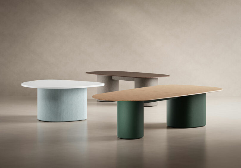 Three modern tables by KFi STUDiOS feature cylindrical bases and oval tops in white, brown, and wood finishes, set against a plain, neutral background.