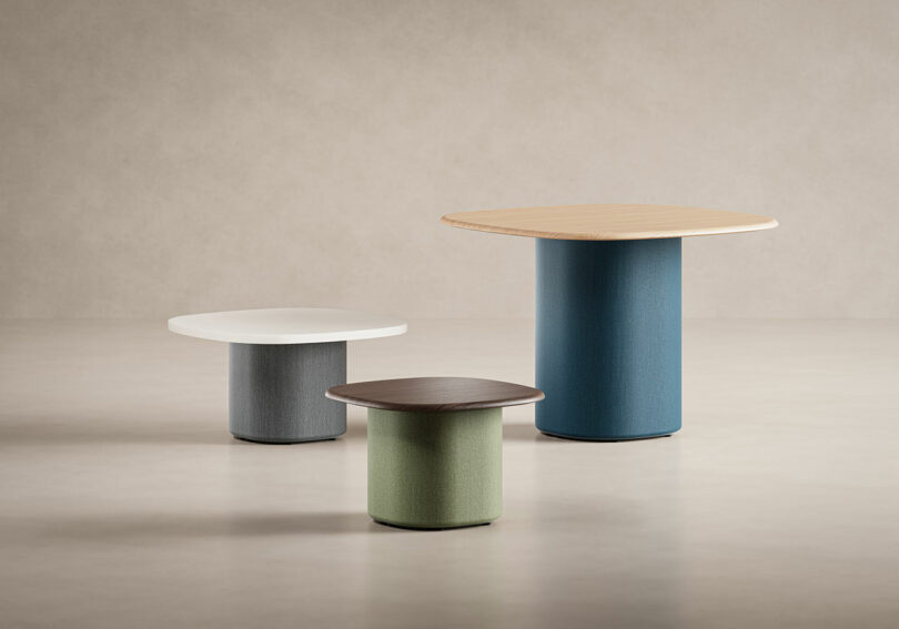 Three modern KFi STUDiOS tables of different heights and colors with cylindrical bases and round or square tabletops are arranged on a neutral background.