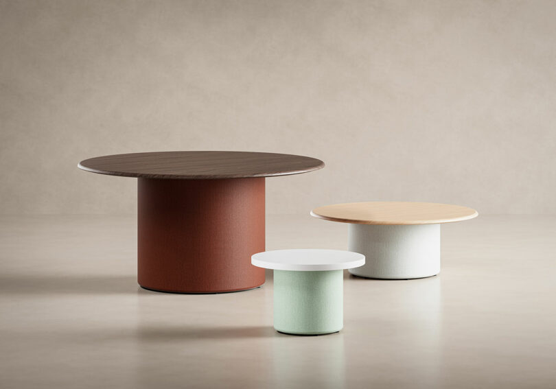 Three round tables from KFi STUDiOS, in varying heights and colors, are arranged on a neutral background; the largest is brown, the medium is light wood, and the smallest is white.