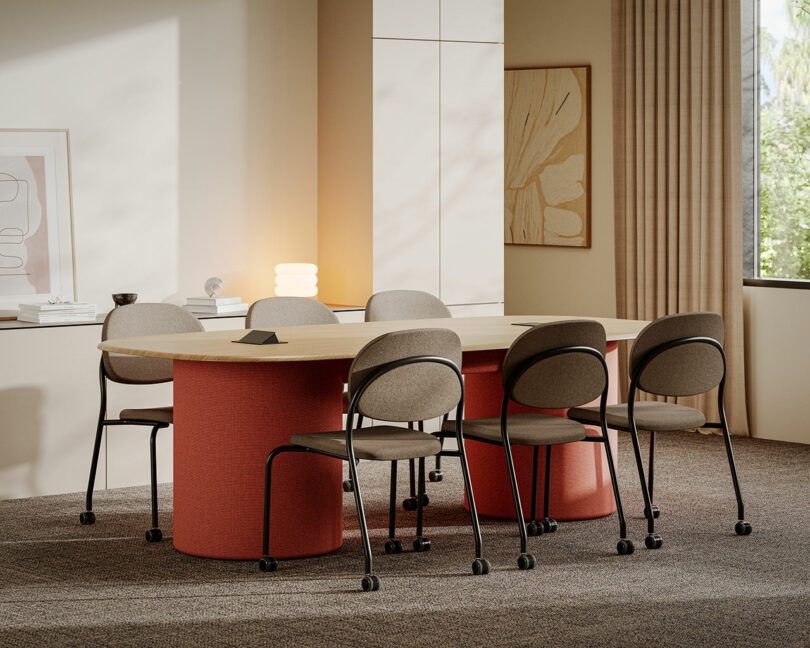 A modern KFi STUDiOS conference room featuring a rectangular wooden table, six cushioned chairs on wheels, neutral decor, and a window adorned with beige curtains.