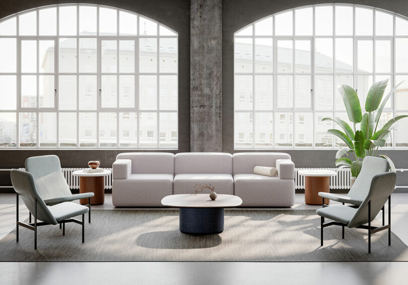 Modern living room by KFi STUDiOS with large arched windows, light gray sofa, two armchairs, a round coffee table, side tables, and a tall potted plant on a neutral rug.