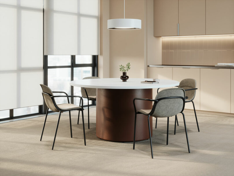 A round table with four chairs by KFi STUDiOS is set in a modern office space with large windows, a pendant light, and beige cabinetry in the background.