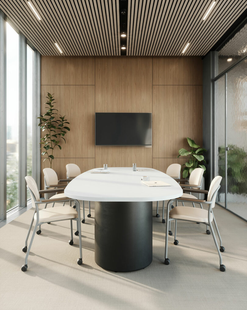 Modern conference room by KFi STUDiOS featuring a large oval table, six chairs, wall-mounted screen, wood panel walls, floor-to-ceiling windows, indoor plants, and neutral decor.