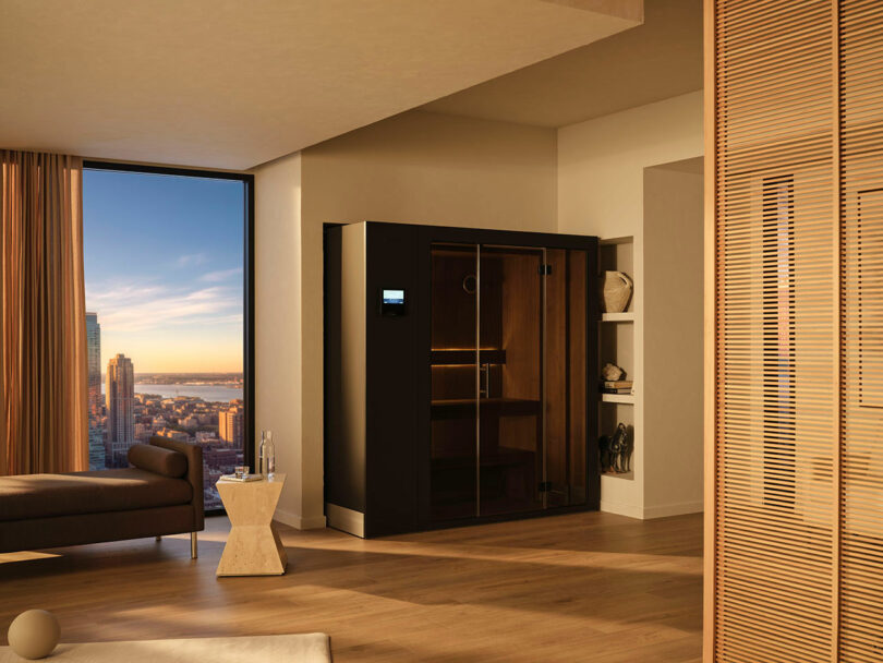 A modern living space with a large window showing a city view, featuring a black home sauna, a lounge chair, and wooden accents.