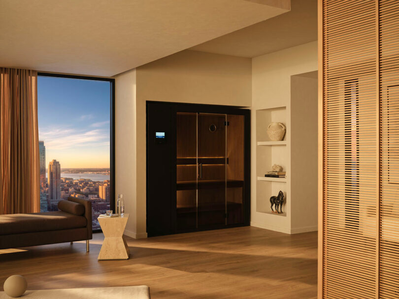 Modern living room with floor-to-ceiling window, city skyline view, wooden flooring, a lounge chair, small side table, built-in shelves, and a black sauna installed against the wall.