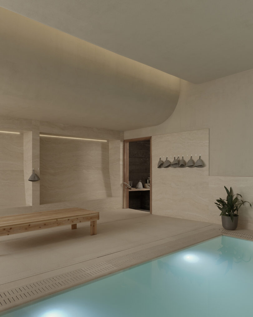 Minimalist indoor pool area with soft beige walls, a wooden bench, wall hooks with towels, a potted plant, and a door leading to a darker room.