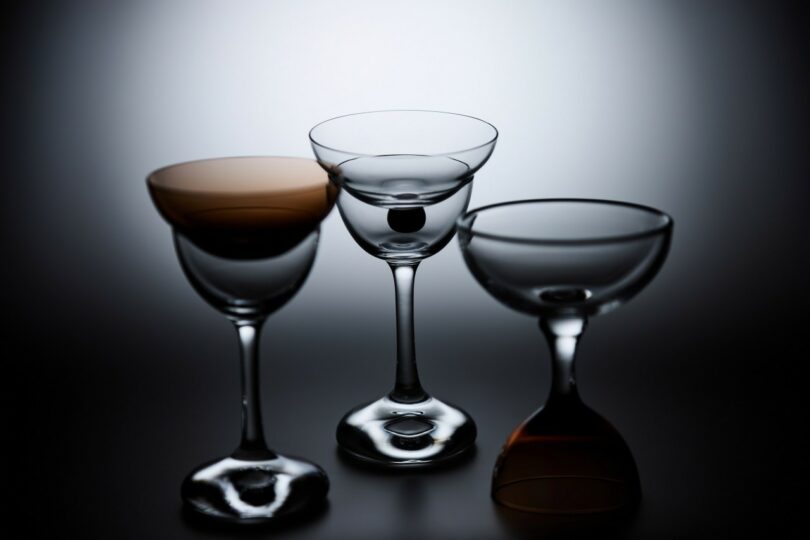 Three glass goblets are arranged on a surface; two are upright and one is upside down. The goblets have a minimalist design with subtle lighting and reflections
