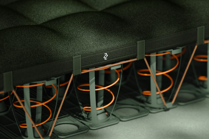 Close-up view of a mattress cross-section showing green cushioning material, orange coil springs, and structural supports underneath.